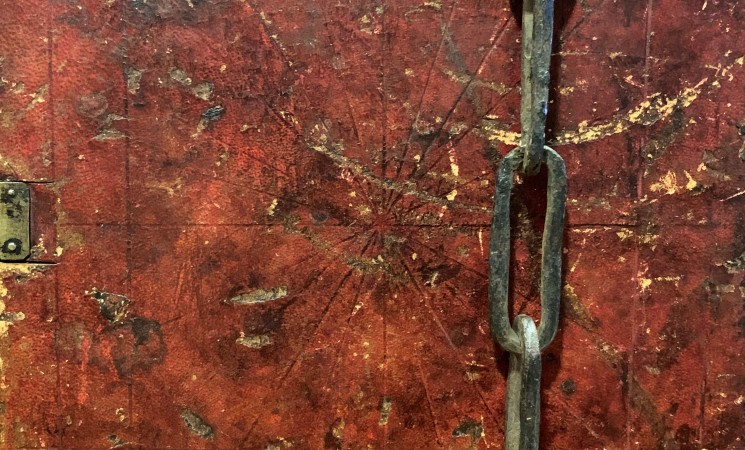 A brownish-red worn leather book cover with an small attached chain.