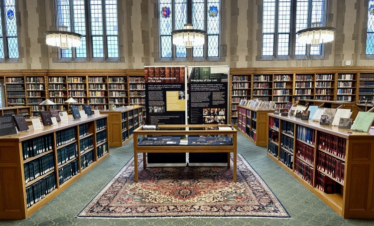 Wideshot photograph of an exhibit case with two posters behind it. Surrounded by bookcases on all sides.