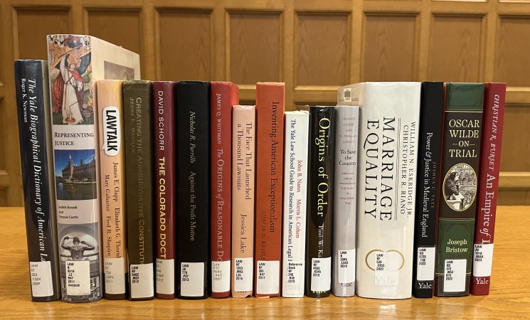 Row of books on top of a wooden table with a wooden wall in the background.