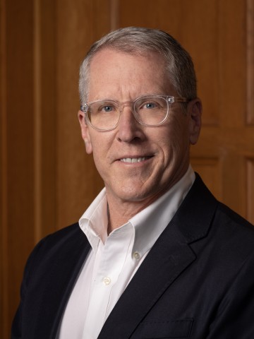A man smiling in front of wood paneling.