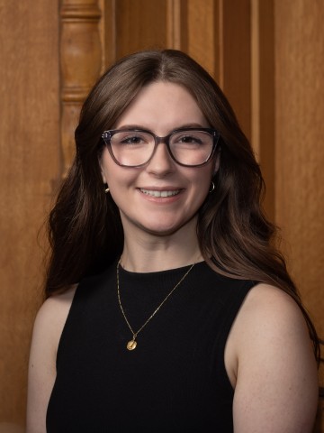 Woman in glass smiling in front of wood paneling. 