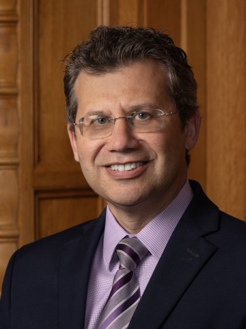 A man in glasses smiling in front of wood paneling.