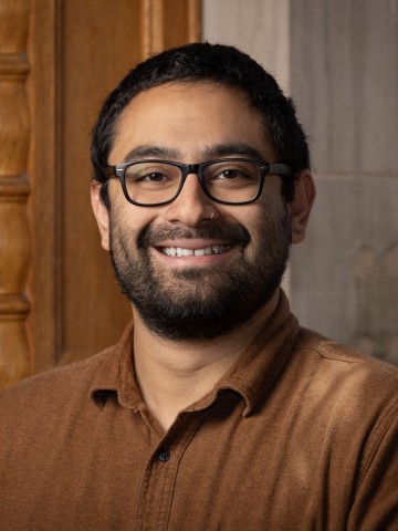 A man smiling in front of stonework and wood.
