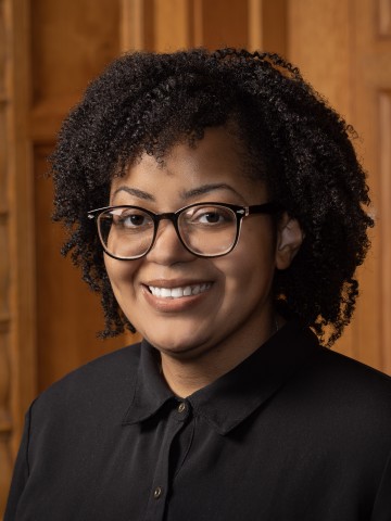 Woman in glass smiling in front of wood paneling.