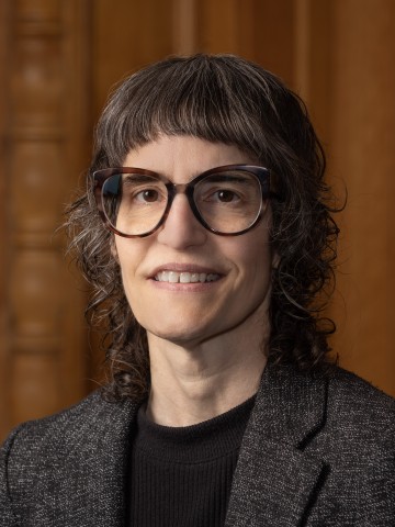 Bespectacled woman smiling in front of wood paneling.