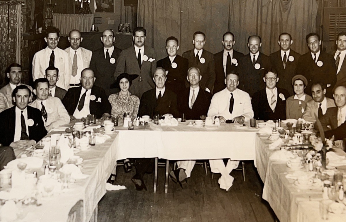 Yellowed photograph of a group of people posing at a dinner