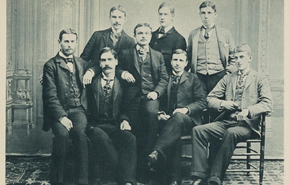 Black and white group photo of eight men looking at the camera