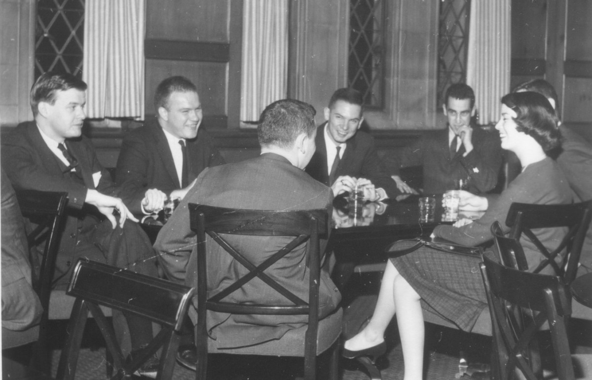 Black and white photo of a group of students, male and female, talking around a table