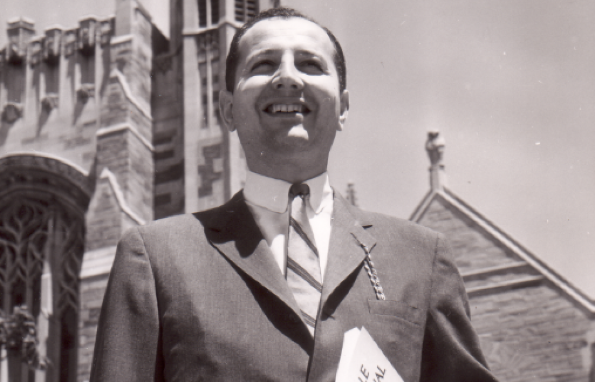 Man in a suit standing in front of a gothic building holding a journal