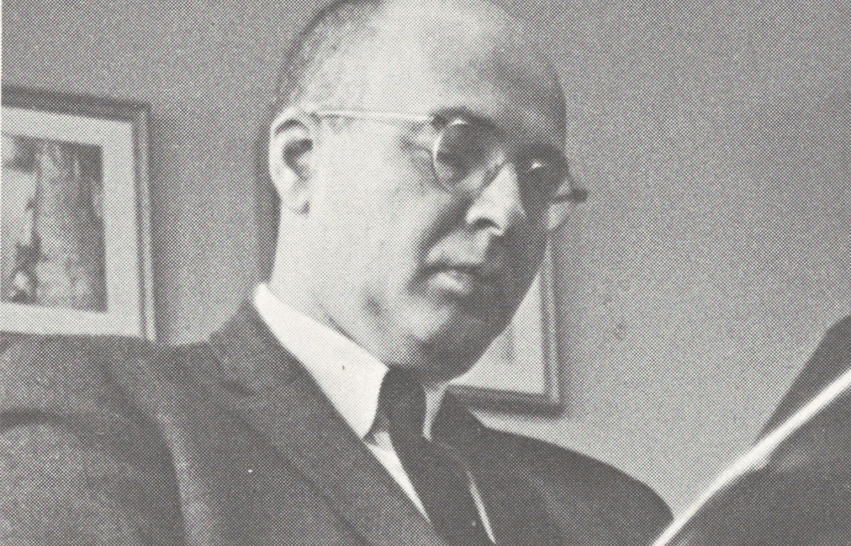 Black and white photograph of a seated man in a suit reading.