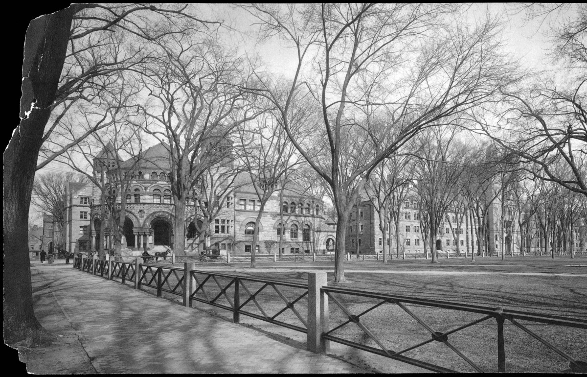 Black and white photograph of the a historical building with a short fence surrounding a courtyard.