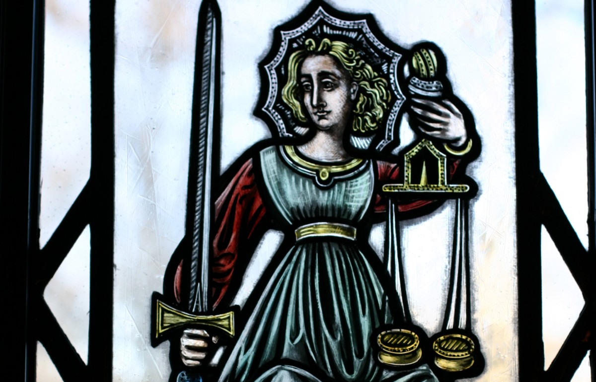 Colored stained glass of Lady Justice holding scales and a sword.