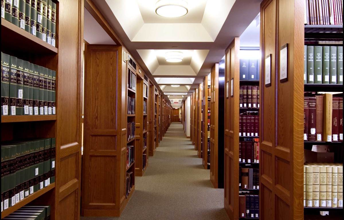 Down-the-hallway photograph of an aisle in the library with book shelves on either side. 