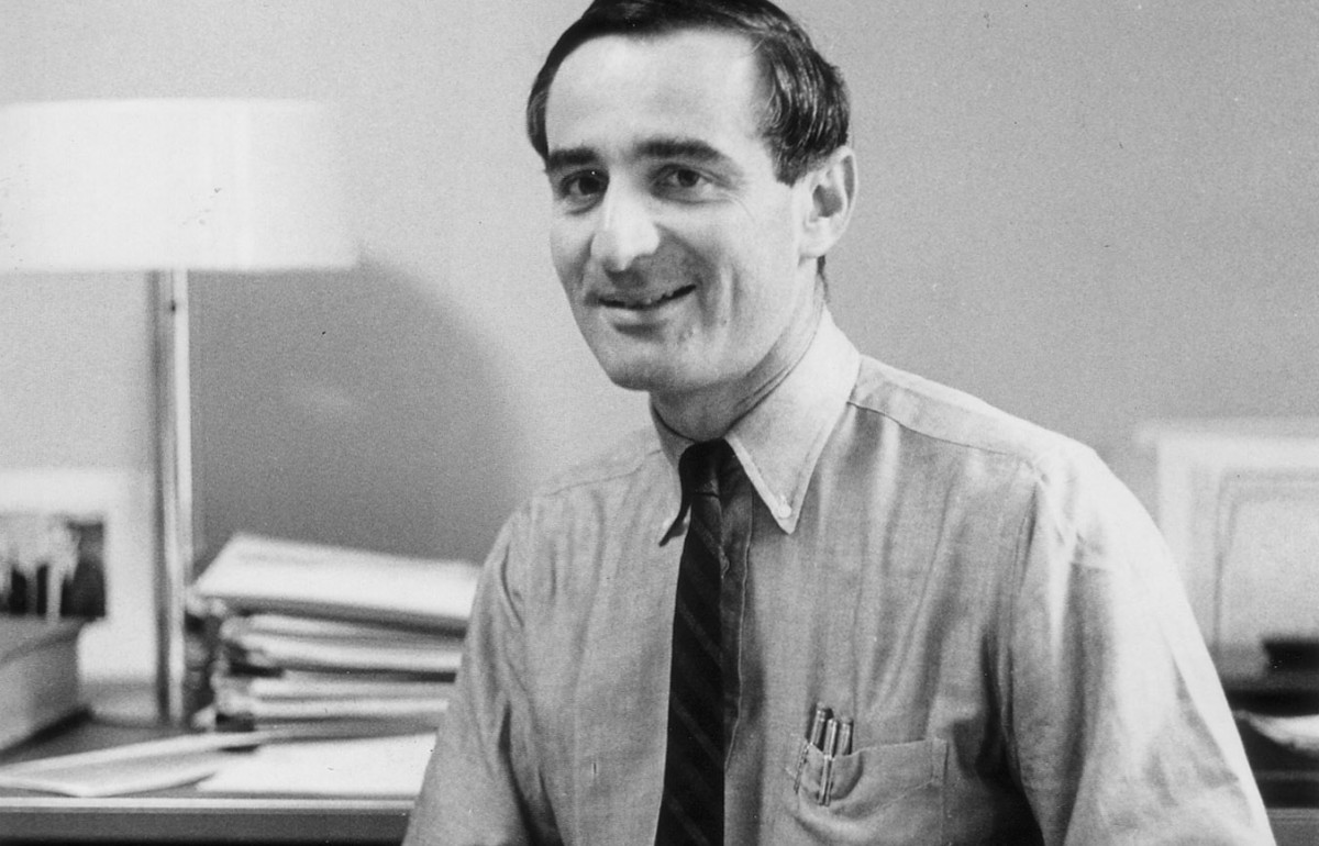 Black and white photograph of a man behind a desk with books and papers around him.