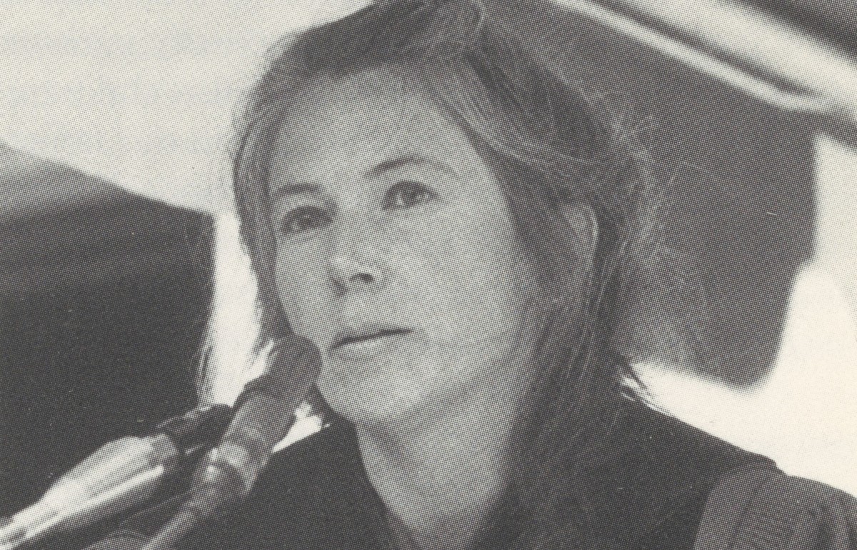 Black and white photograph of a woman in graduation robes speaking at a podium.
