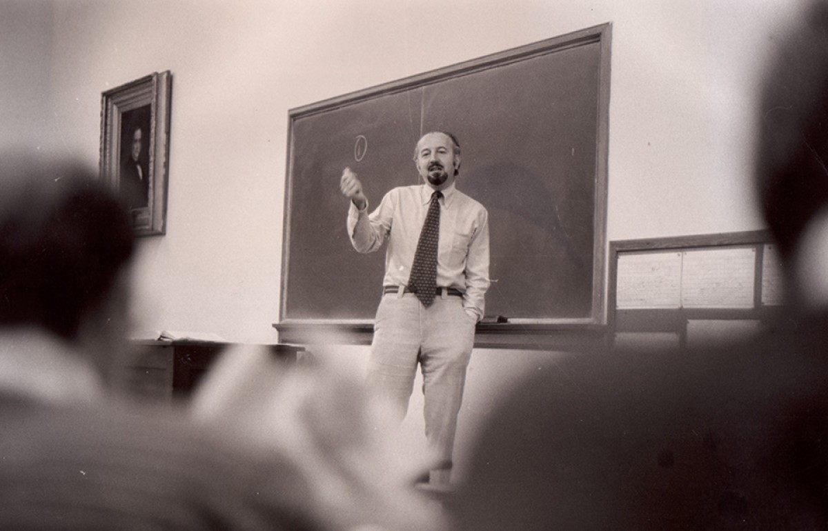 Photograph of a man holding chalk teaching in front of a chalkboard.