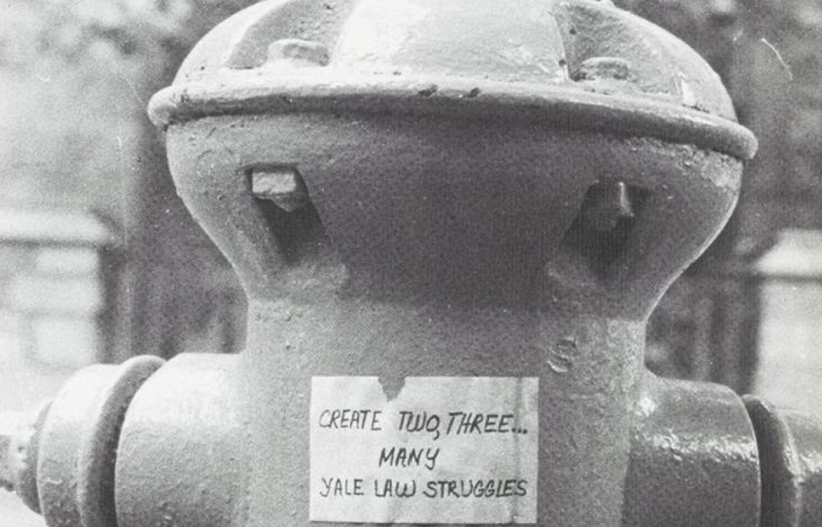 Black and white photo of a fire hydrant with the piece of paper on it saying "Create two, three...many yale law struggles"