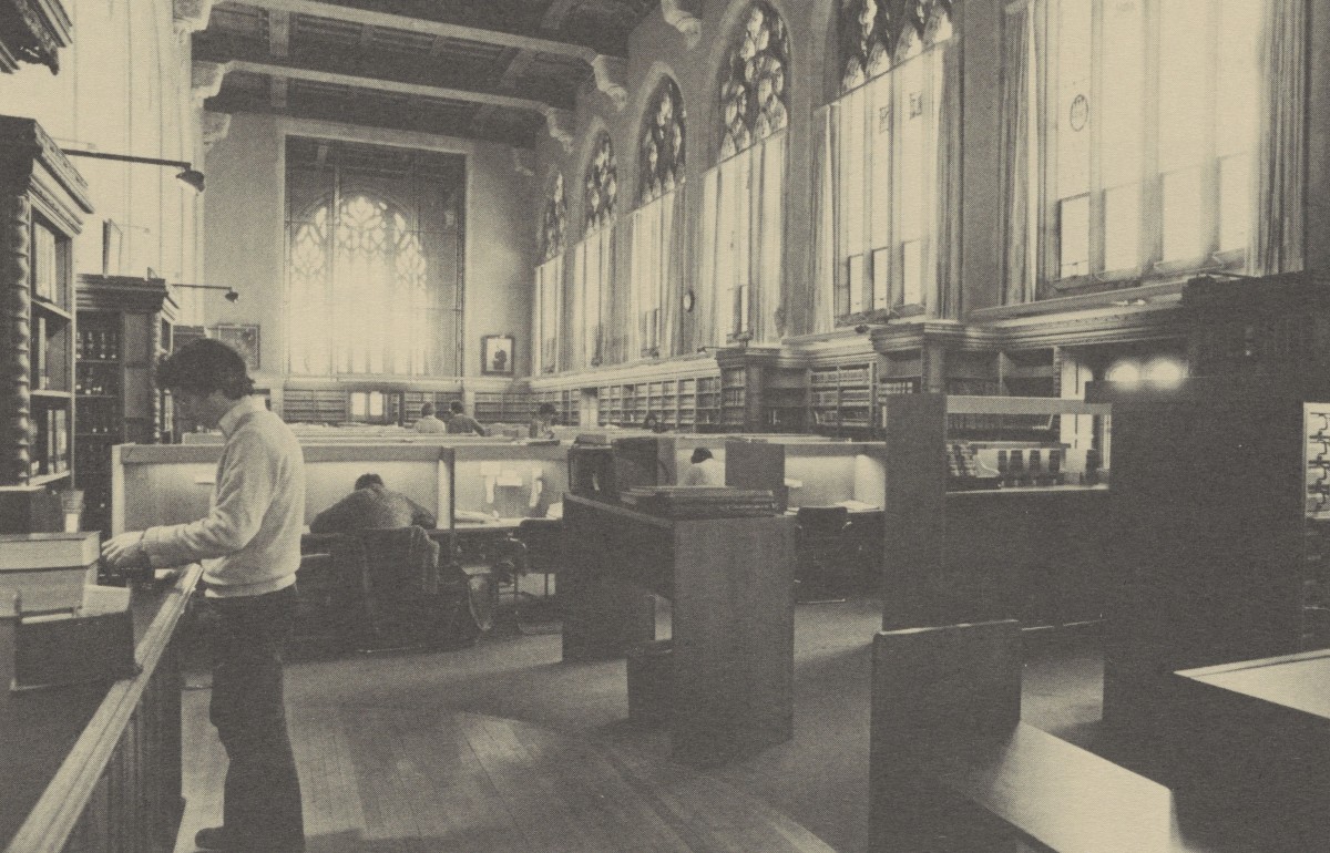 Student reading at a standing desk in the library reading room, surrounded by carrels. 