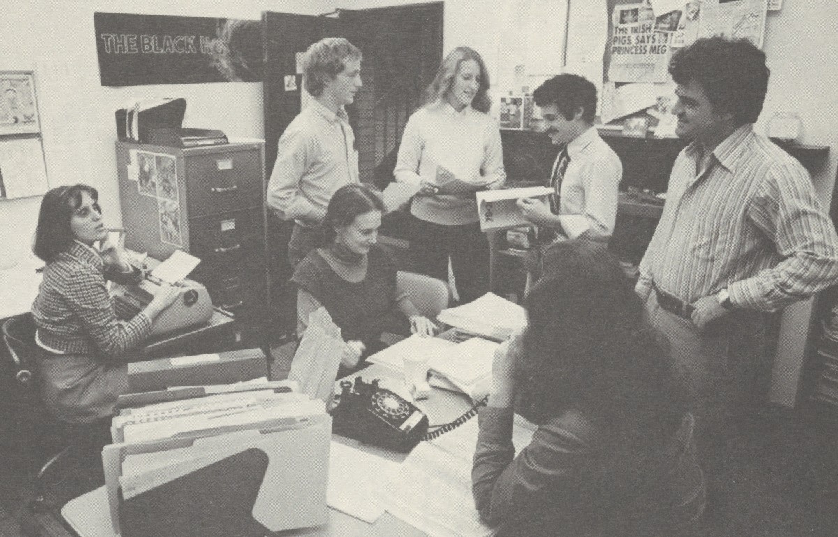 Yellowed photograph of a group of students in a small office, surrounded by paperwork.