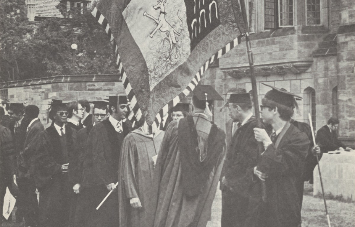 Parade of graduates with first one holding a flag with Yale Law's coat of arms