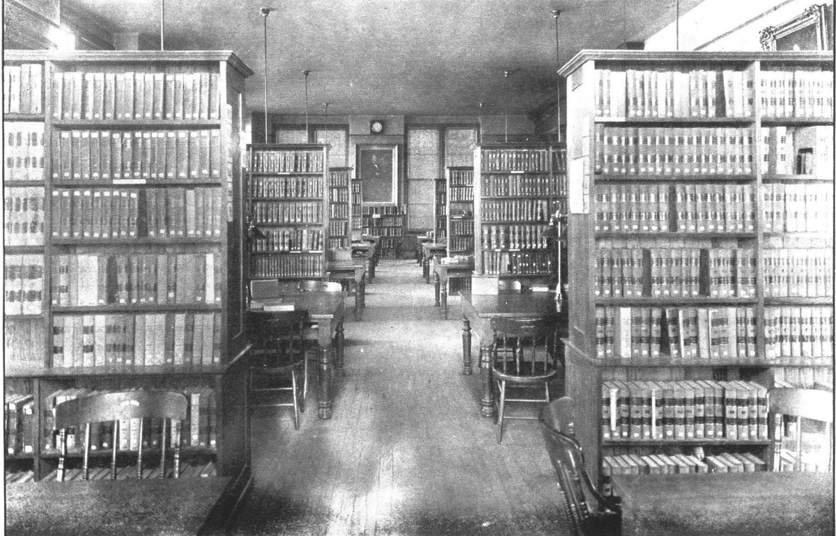 Faded black and white photograph down a corridor with shelves of books on both sides.